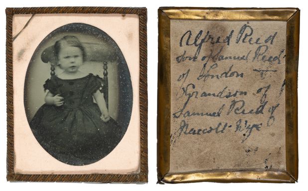 A framed ambrotype of a young boy in a dress sitting on a high back chair
