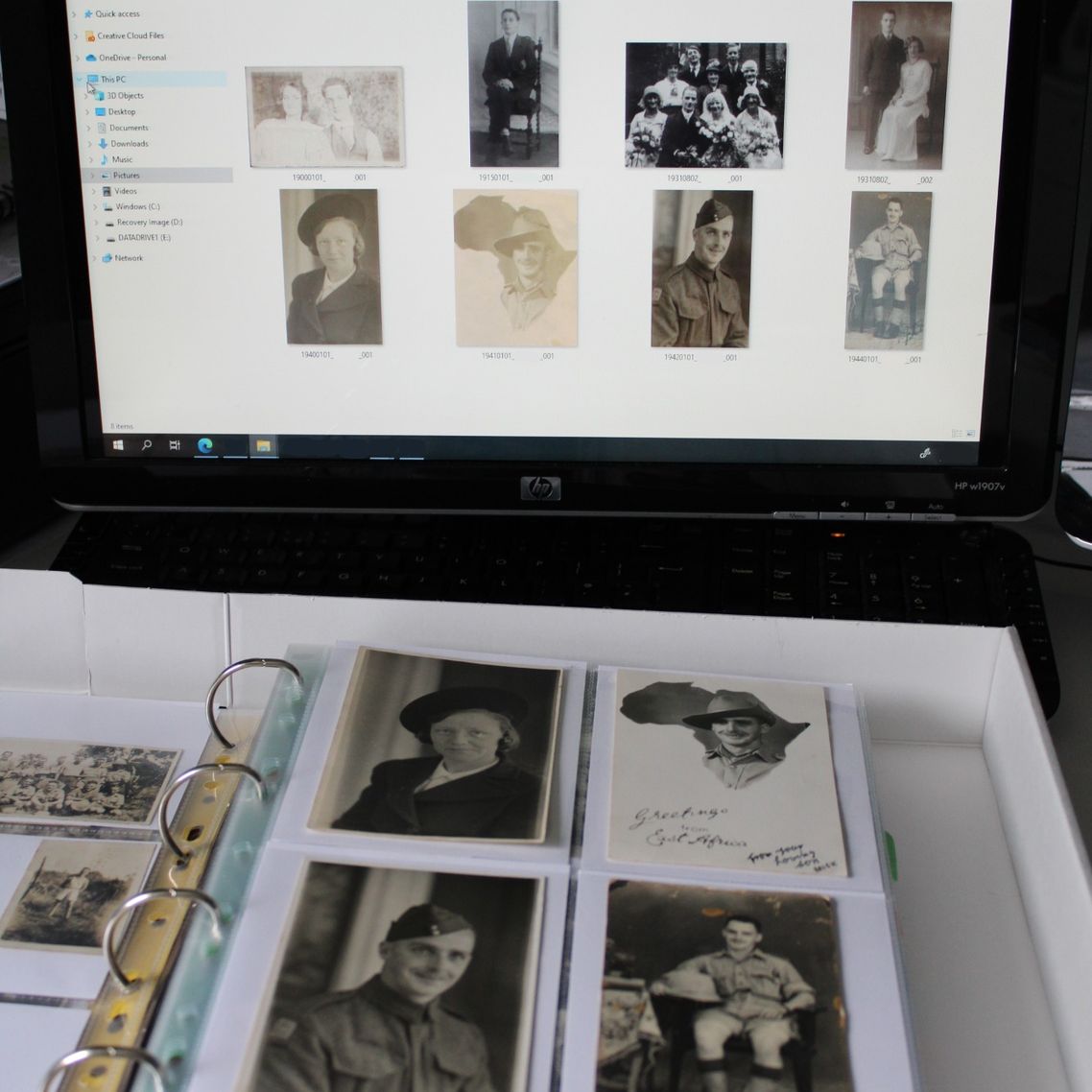 A ring box-binder containing old photos in front of a computer screen displaying the digital versions